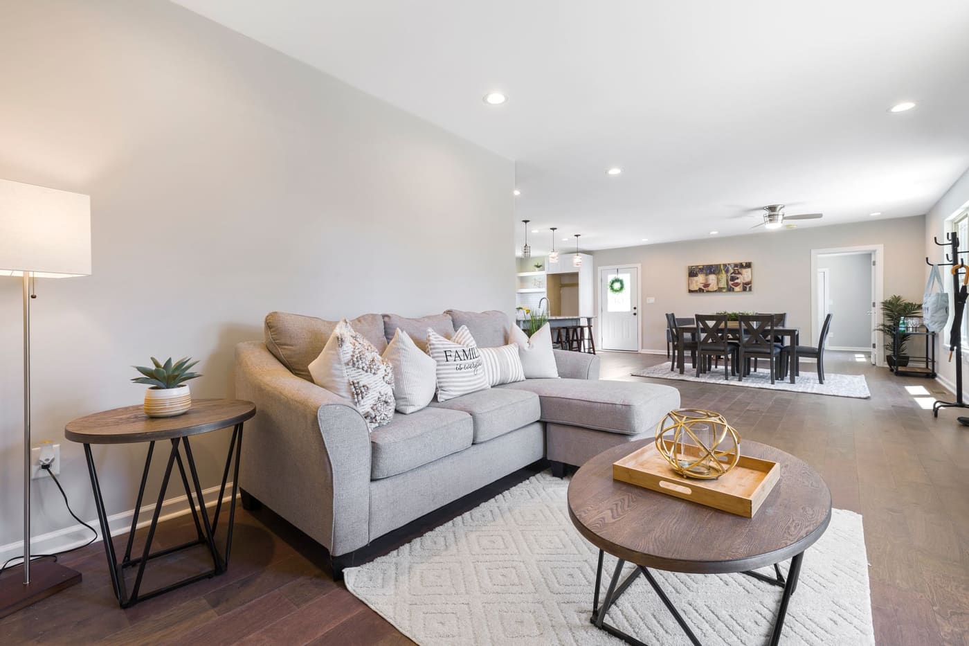 Bright open living room with a gray sofa, a round coffee table and a dining table in the background