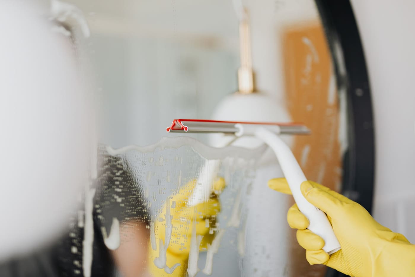 Gloved hand pulling a squeegee across a wet bathroom mirror