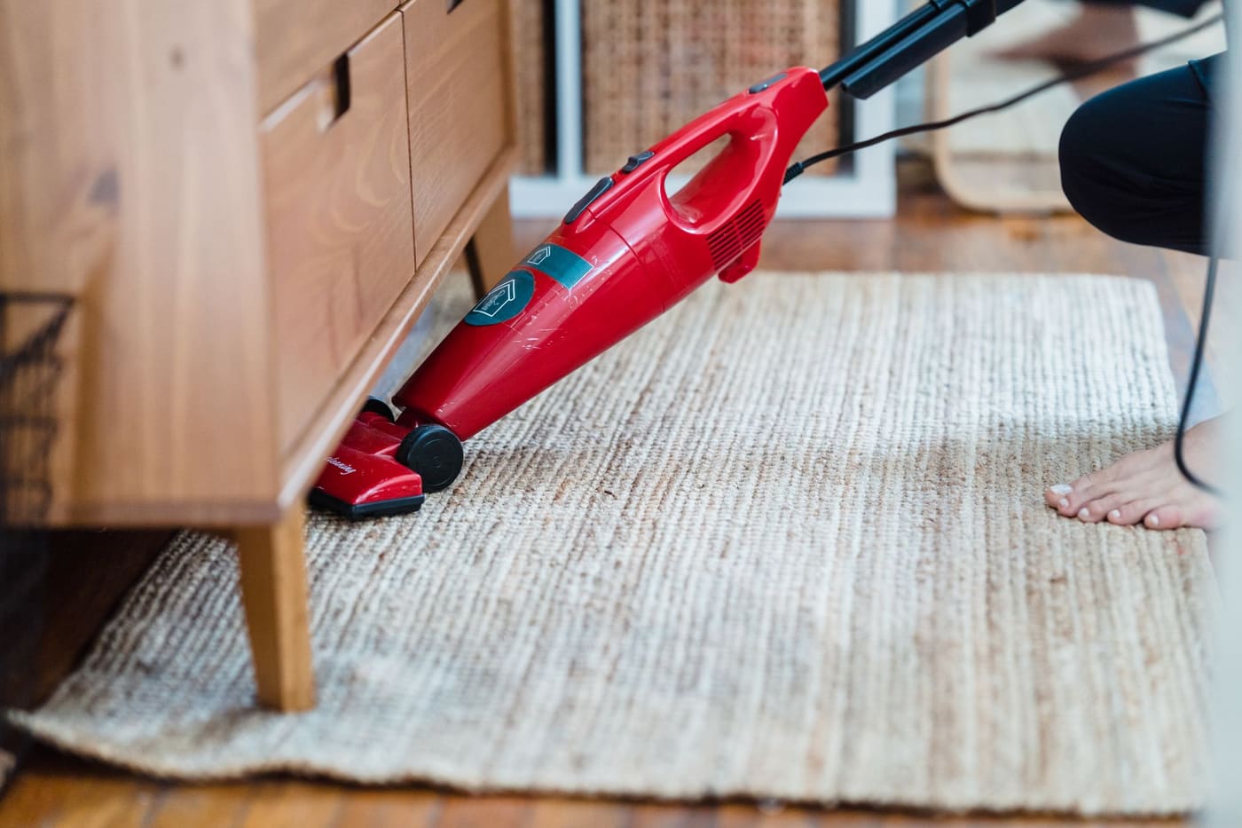 Red handheld vacuum cleaning a woven rug under a wooden cabinet