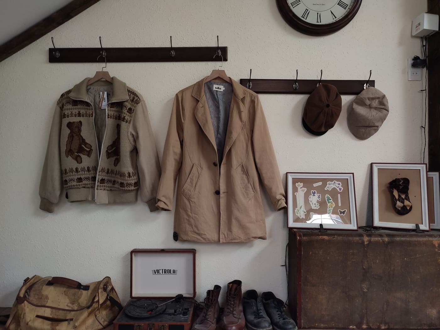 Wall-mounted hooks holding a jacket, a coat and two hats above a wooden chest